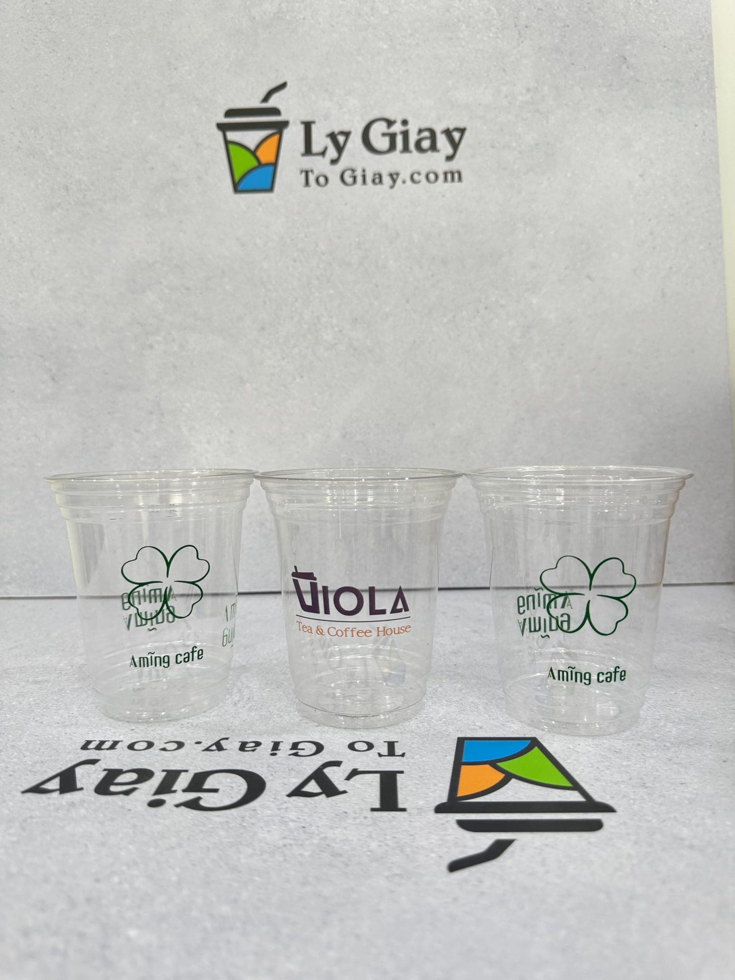 Three clear 12 oz PET cups printed with cafe logos, on the studio backdrop