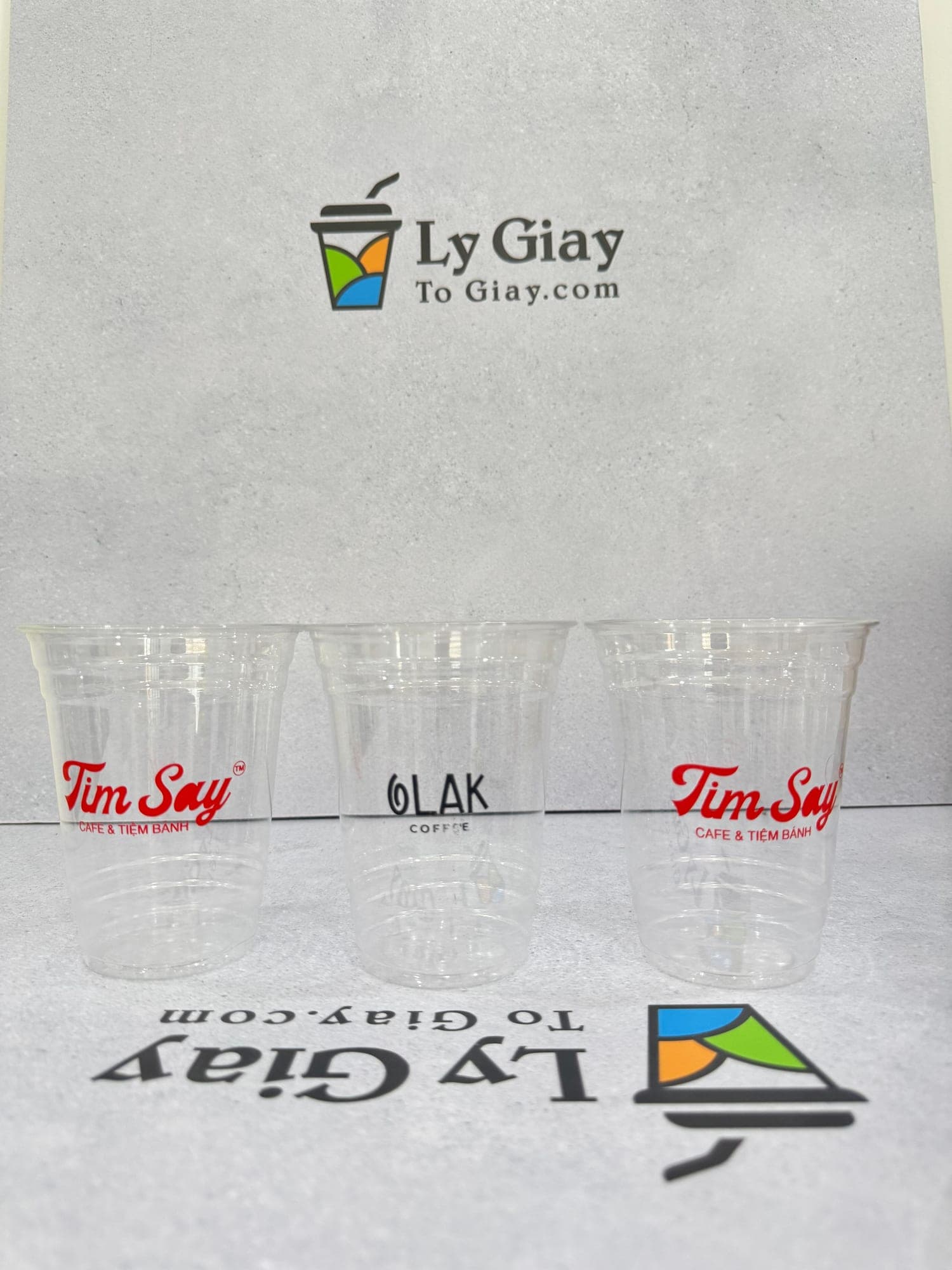 Three clear 16 oz PET cups printed with cafe logos, on the studio backdrop